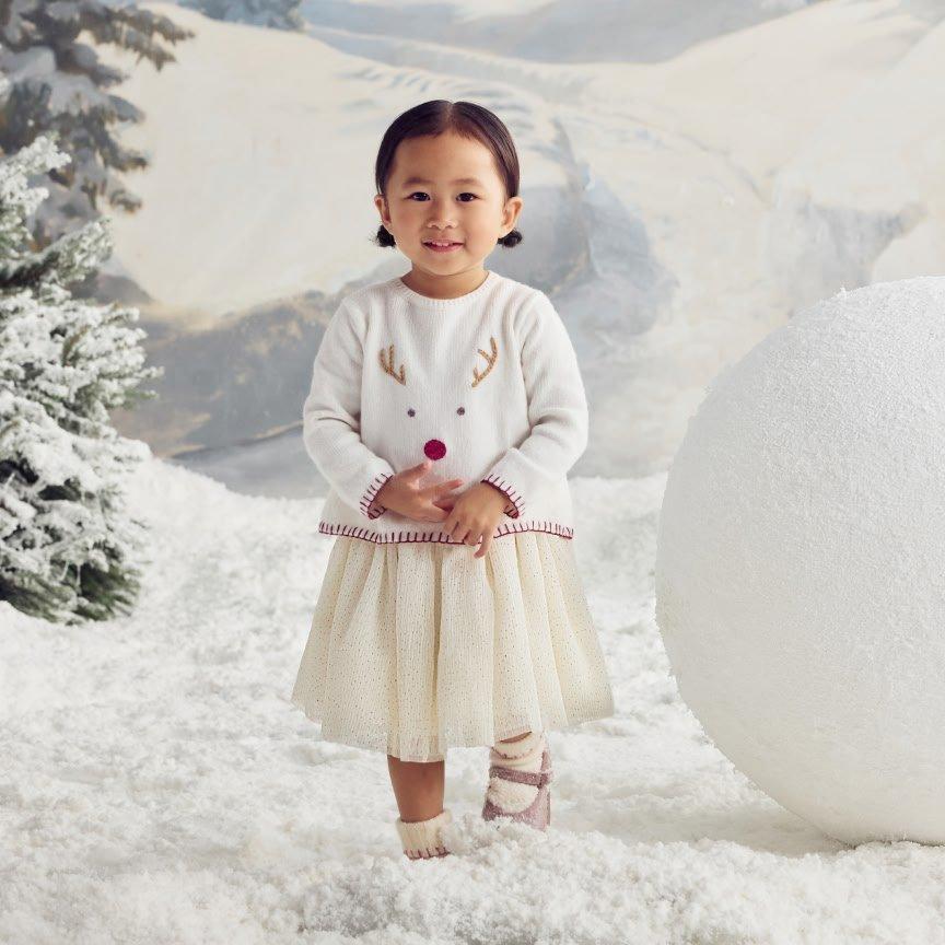 a little girl standing in the snow with a reindeer ornament